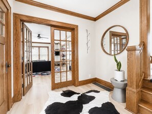 Ein Zimmer mit Holzboden, einem Kuhfellteppich, einem runden Spiegel und einer Treppe mit Holzwangen.