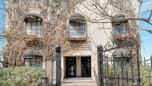 Ein Gebäude mit schmiedeeisernem Tor, Stufen, die zu einer Tür führen, und einem Balkon mit Geländer.