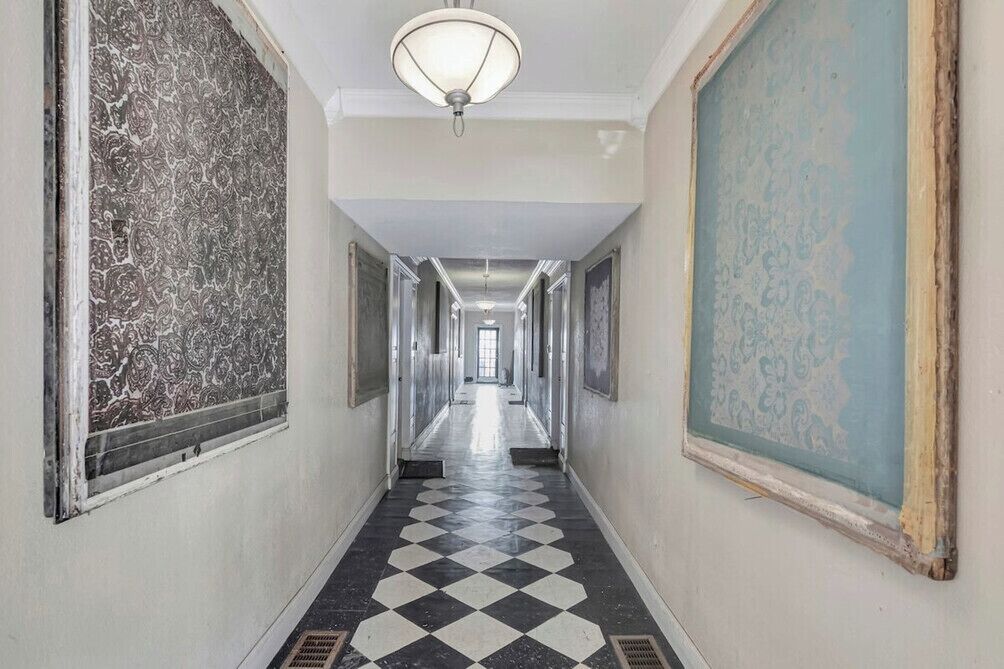 A long hallway with patterned walls, a checkered floor, and a light fixture at the end.