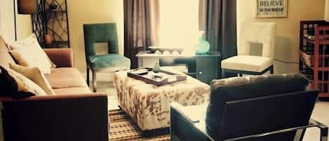 Un salón con sofá, sillón, reposapiés y una decoración de cabeza de ciervo. Se observa una pared con citas motivacionales y una ventana con cortinas.