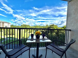 A balcony with a table and chairs, a vase with flowers, and a view of a golf course and buildings. - Spacious 2BR Condo in the Heart of Pigeon Forge (Pigeon Forge)
