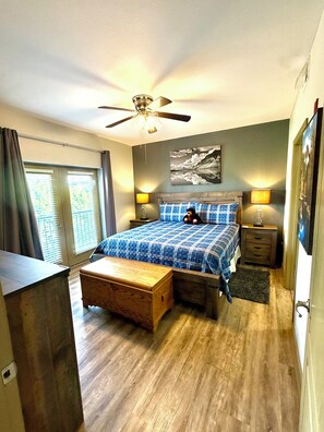 A bedroom with a bed, a wooden bench, a ceiling fan, a nightstand, a lamp, and a window with curtains. - Spacious 2BR Condo in the Heart of Pigeon Forge (Pigeon Forge)