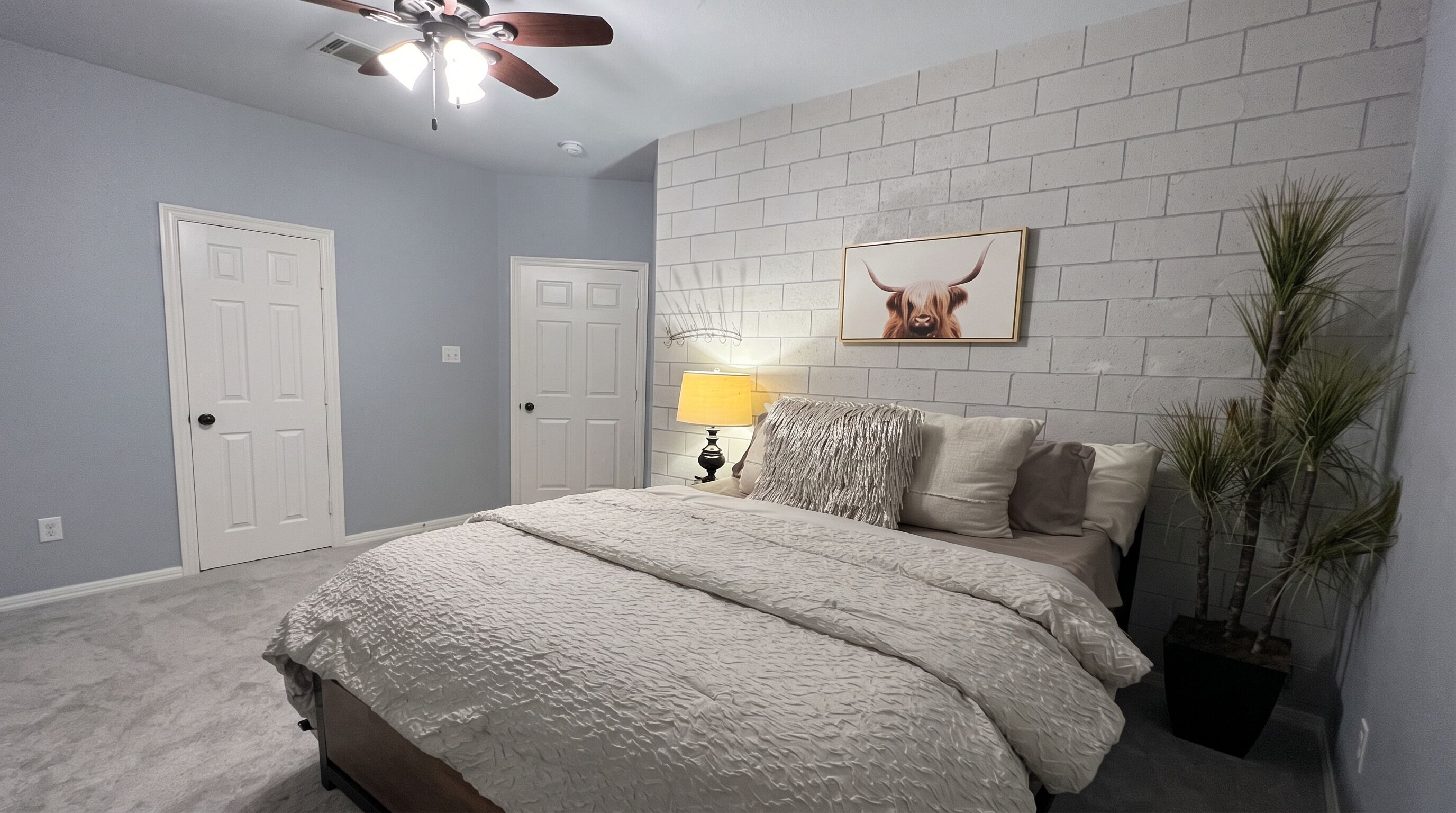 A bedroom with a bed, a ceiling fan, a wall-mounted lamp, and a framed picture.
