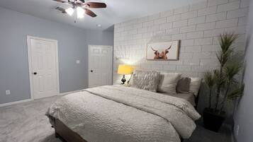 A bedroom with a bed, a ceiling fan, a wall-mounted lamp, and a framed picture.