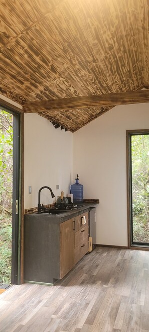 Eine Küche mit Holzbalkendecke, einem großen Wasserspender und Blick auf grüne Umgebung.