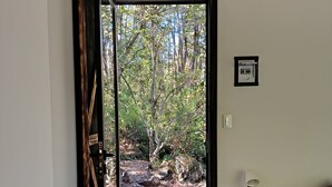 Ein Zimmer mit Holzbalkendecke, einem Bett mit grüner Bettdecke, einem Nachttisch mit Lampe und Blick auf eine natürliche Landschaft durch eine offene Tür.