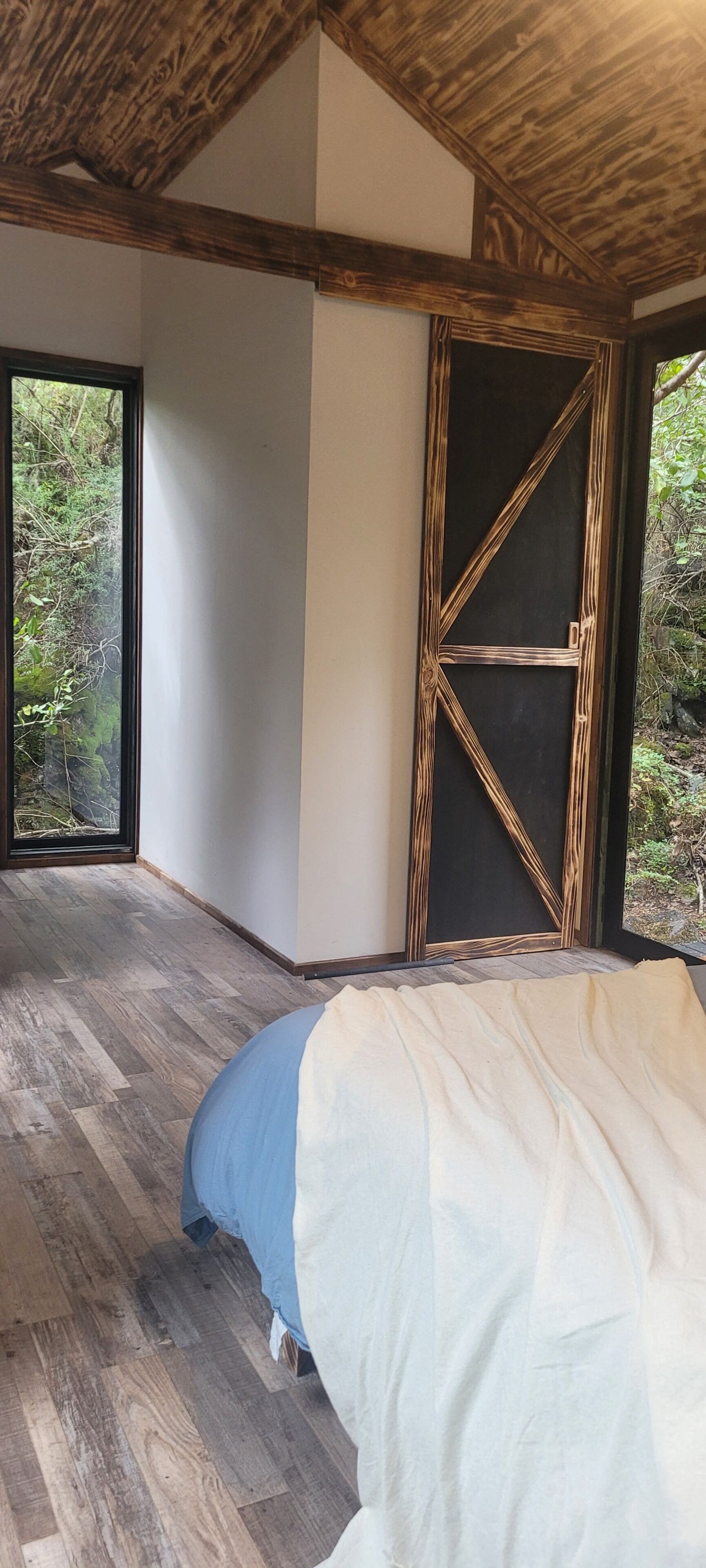 Una habitación con una cama, un ventanal grande y techo de madera.
