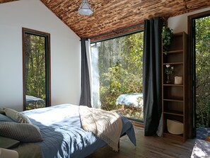 Ein Schlafzimmer mit großem Fenster, einem Bett, einer Holzbalkendecke und einem Bücherregal.
