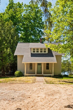 A single-story house with a front porch, a chimney, and a clear view of the surrounding trees.