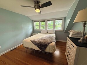 Ein Schlafzimmer mit Bett, Deckenventilator, Fenster mit Aussicht, Nachttisch und Kommode.