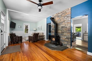 A living room with a stone fireplace, wooden flooring, and a ceiling fan.
