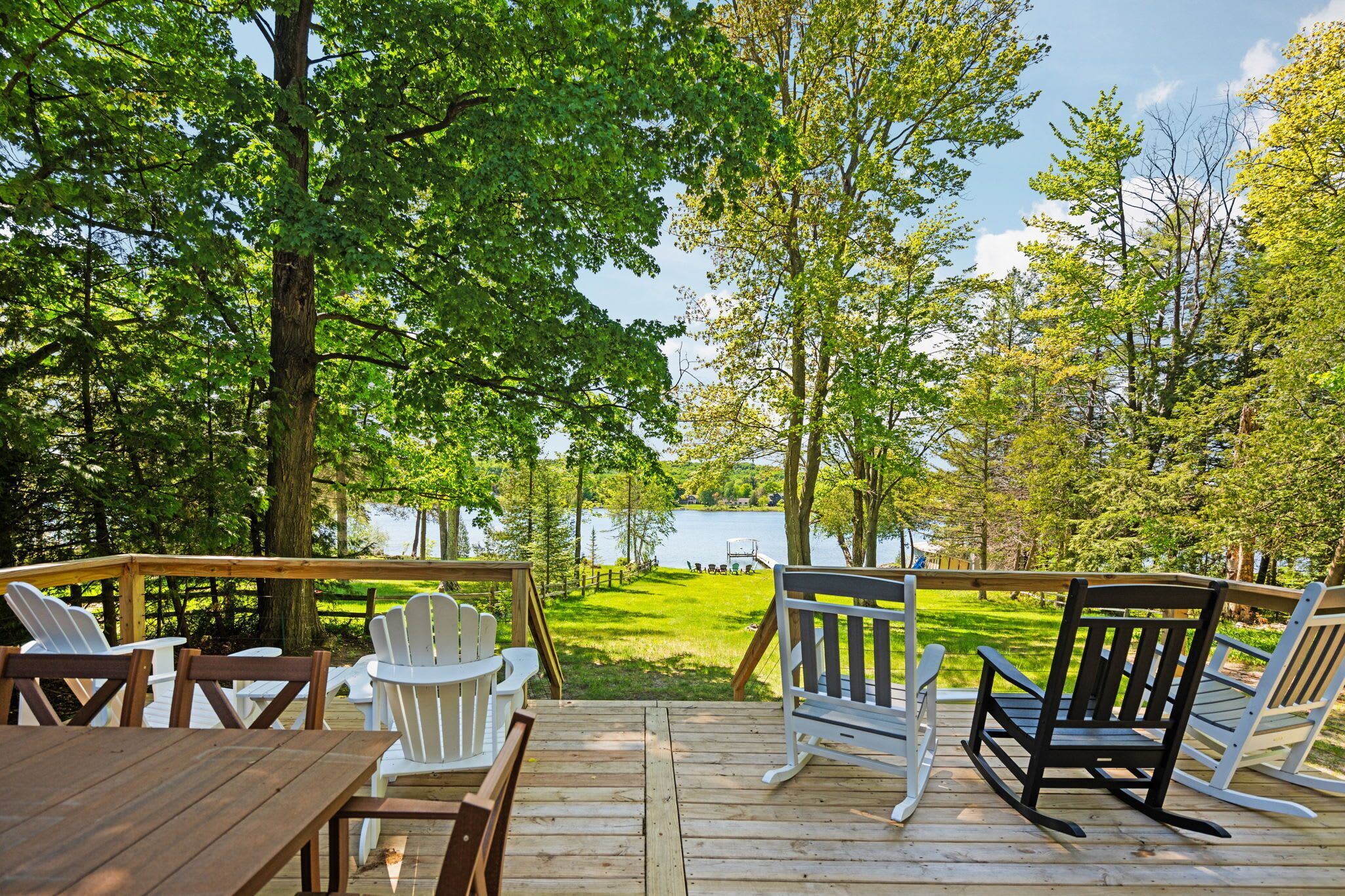 A wooden deck with outdoor furniture, overlooking a lake and surrounded by trees.