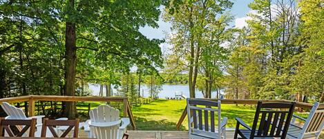 A wooden deck with outdoor furniture, overlooking a lake and surrounded by trees.