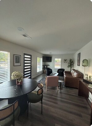 Ein Wohnzimmer mit Esstisch, Stühlen, einer Couch und einem Fernseher.