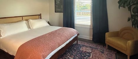 A bedroom with a bed, a ceiling fan, a window with curtains, a chair, and a plant.