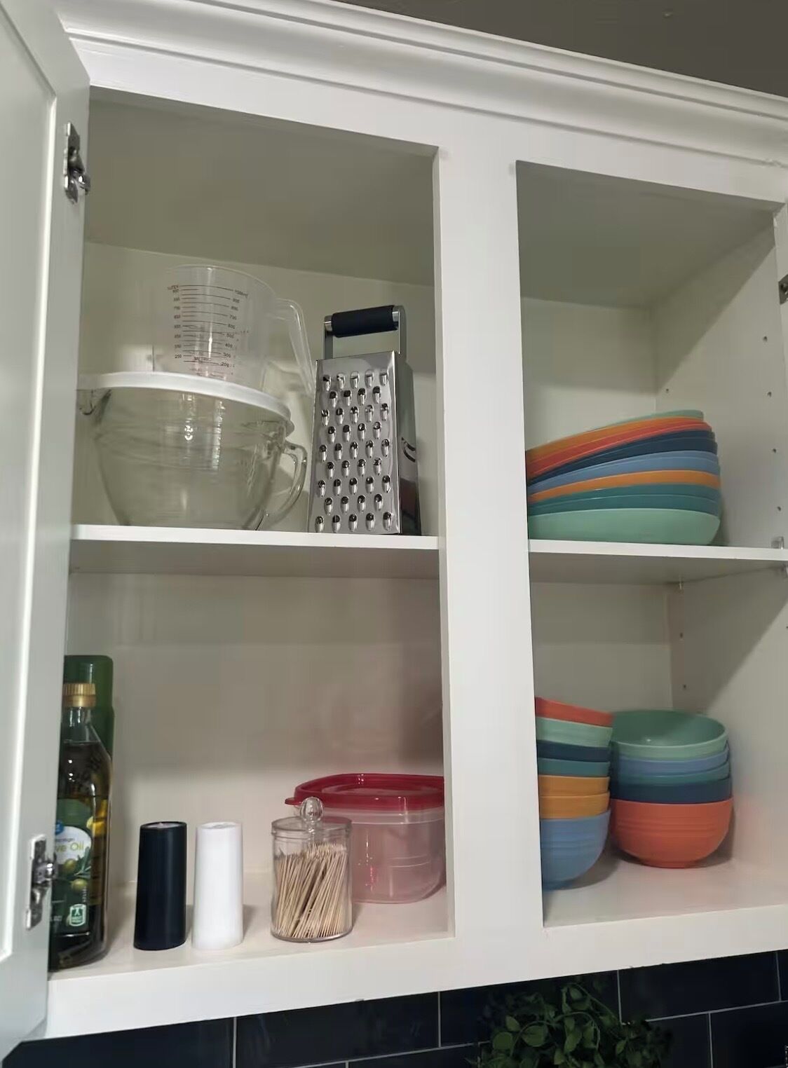 Ein Küchenschrank mit Messbecher, Reibe und bunten Schüsseln.