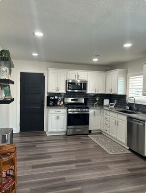 A modern kitchen with white cabinets, stainless steel appliances, and a dark wood floor. - Cozy 2 bedroom home close to downtown Frisco! Enjoy all that Frisco has to offer (Frisco)
