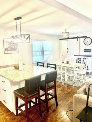 A kitchen with a central island, dining area with chairs, a clock, and a sign that reads 'Home Sweet Home.' - Near McLeod & Downtown · Sleeps 6 · Free WiFi (Florence)