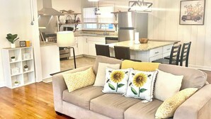 A living room with a beige sofa, wooden flooring, a ceiling fan, and a kitchen in the background. - Near McLeod & Downtown · Sleeps 6 · Free WiFi (Florence)