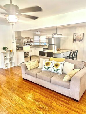 A living room with a beige sofa, wooden flooring, a ceiling fan, and a kitchen in the background. - Near McLeod & Downtown · Sleeps 6 · Free WiFi (Florence)