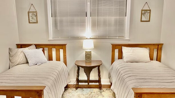 A bedroom with two single beds, a small table with a lamp, and a window with blinds. - Near McLeod & Downtown · Sleeps 6 · Free WiFi (Florence)