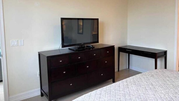 Un dormitorio con cama, cómoda, televisor y escritorio.