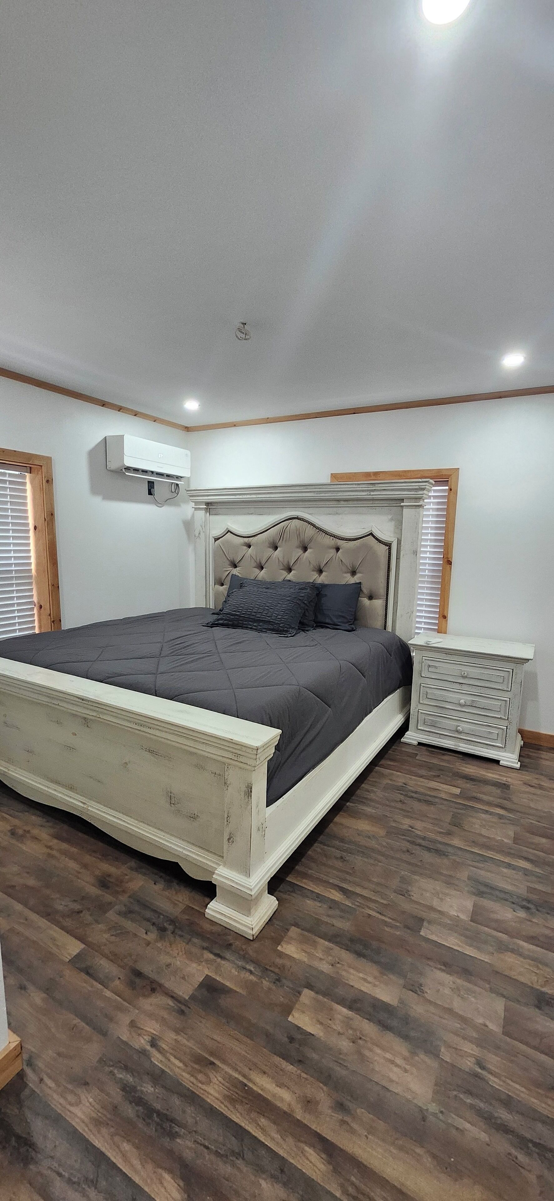 A bedroom with a large bed, a nightstand, and an air conditioning unit.