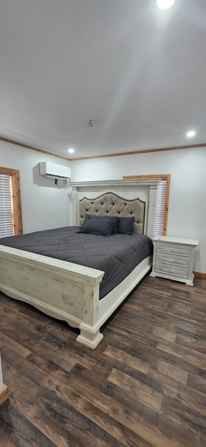 A bedroom with a large bed, a nightstand, and an air conditioning unit.