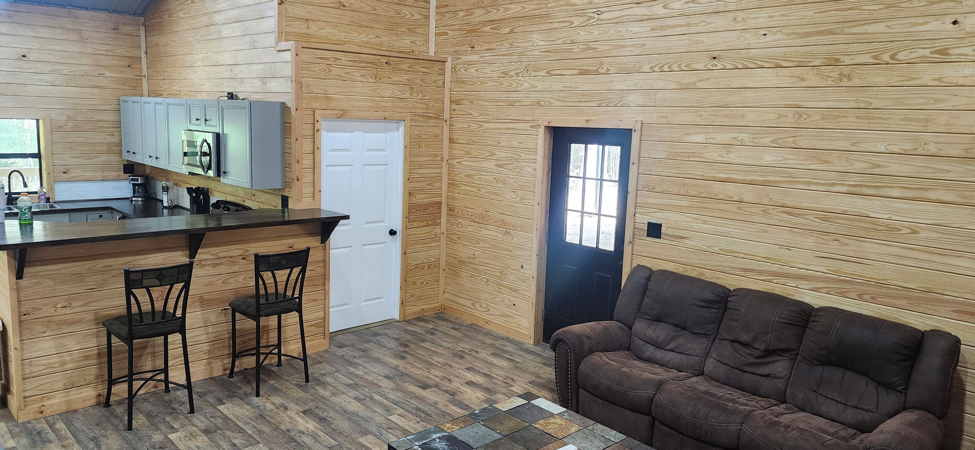 A compact kitchen with a bar area, a door, and a seating area with a couch.