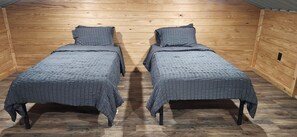 A small, wooden-paneled room with two single beds, each with a grey quilted bedspread and matching pillows.