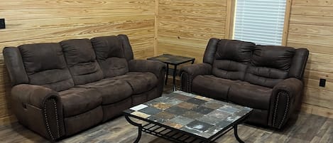 Una habitación con paredes de madera, dos sofás marrones, una mesita y un equipo de aire acondicionado.