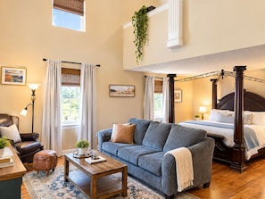 A bedroom with a four-poster bed, a sofa, a coffee table, and a view of the outdoors. - The Woodrow House (Lubbock)