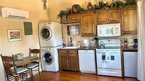 Una cocina compacta con armarios de madera, lavadora, microondas, lavavajillas y un comedor con mesa y sillas.