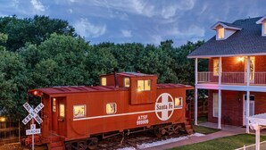 A train caboose with 'Santa Fe' branding and a house with a balcony. - The Woodrow House (Lubbock)