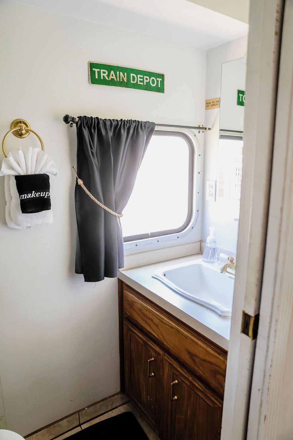 Un baño pequeño con un lavamanos, toallero con una toalla de maquillaje, una cortina y un letrero que dice 'TRAIN DEPOT'.