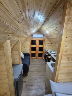A compact wooden room with a bed, a small table, and a kitchenette.