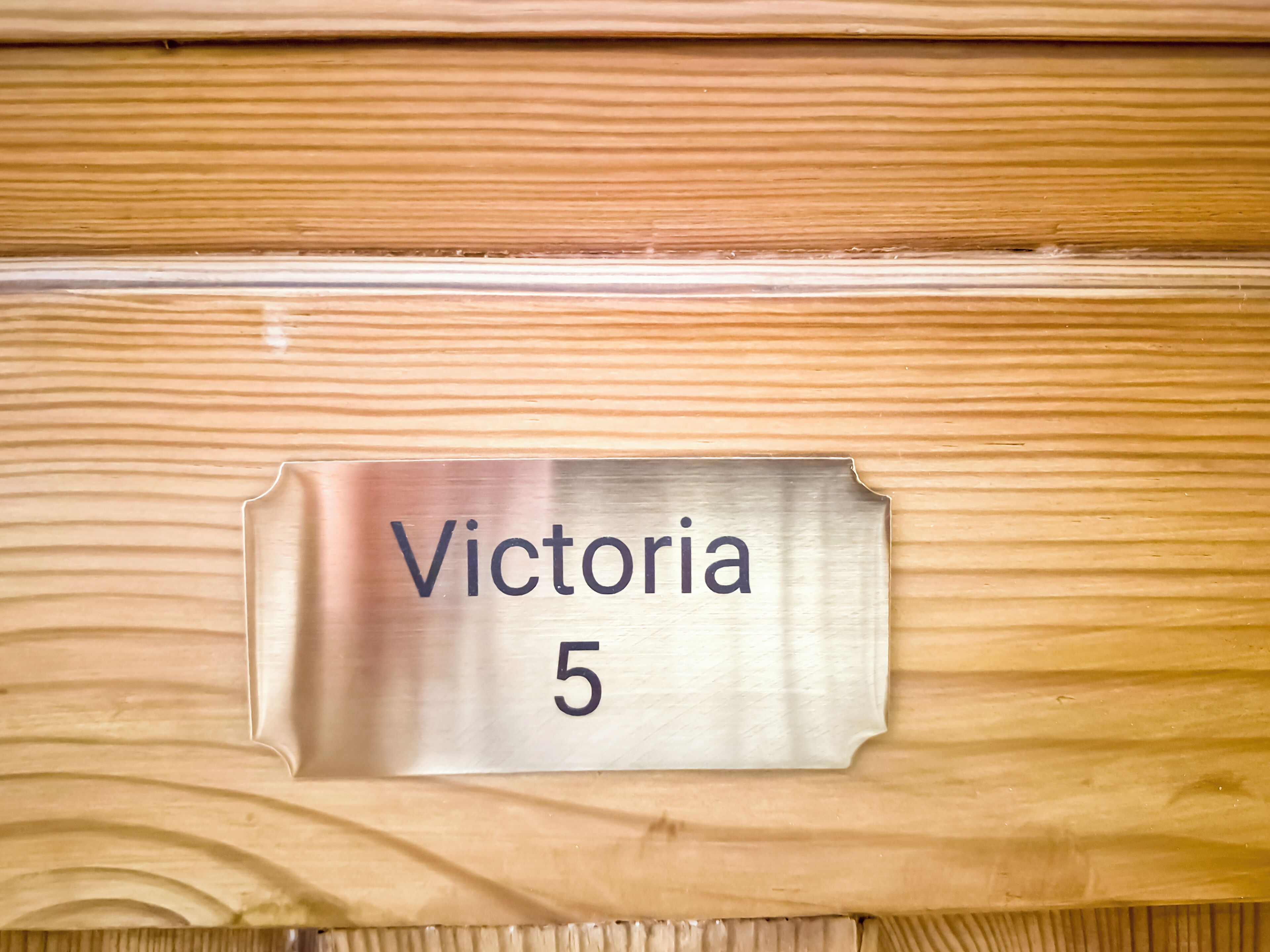 Una placa metálica con el número de habitación 'Victoria 5' sobre una superficie de madera.