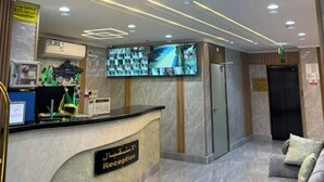 Zona de recepción de un hotel con suelo de mármol, mostrador de recepción, pantalla de televisión y un sofá.