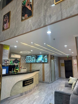 A hotel reception area with a marble floor, a reception desk, a television screen, and a couch. - Manazil Rud (Makkah)
