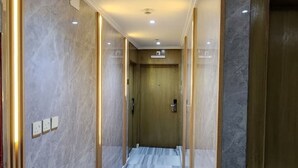 Un pasillo con suelo de mármol, una puerta de madera al fondo e iluminación empotrada.