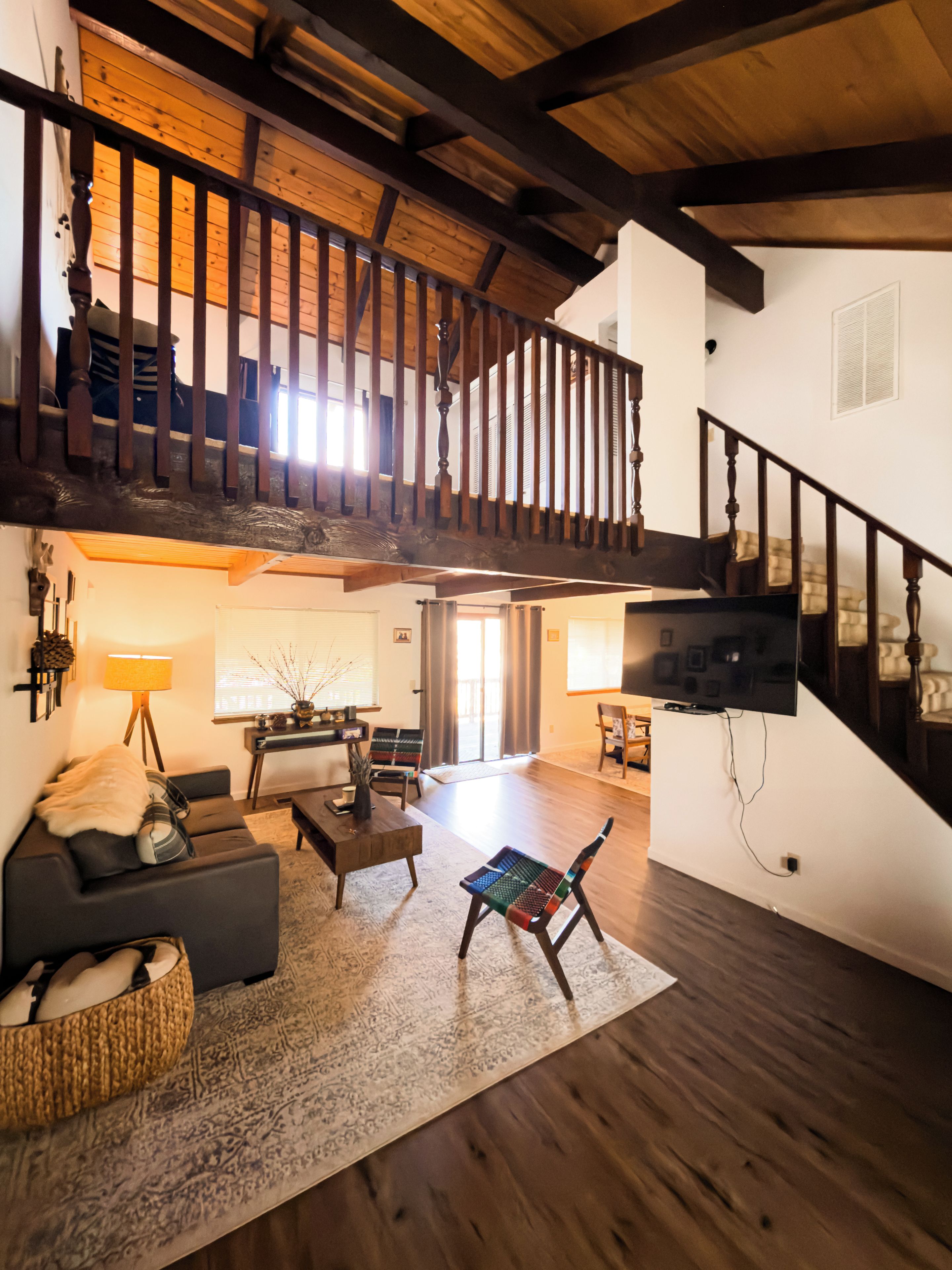 Un vaste espace de vie doté d’un plafond haut, de poutres en bois, d’un escalier et d’un téléviseur à écran plat fixé au mur.