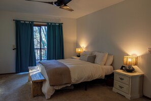 A bedroom with a bed, bedside lamps, a bench, and a view through a window with curtains. - A magical cabin located in -The "Gateway to Yosemite" (Groveland)