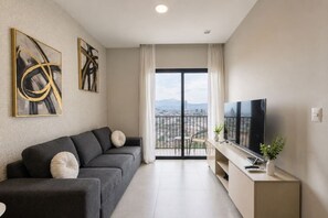 A modern living room with a grey sofa, a flat-screen TV, and a balcony with a city view. - ¡Luxury in Centro! Parking, Gym - 3 people (Monterrey)