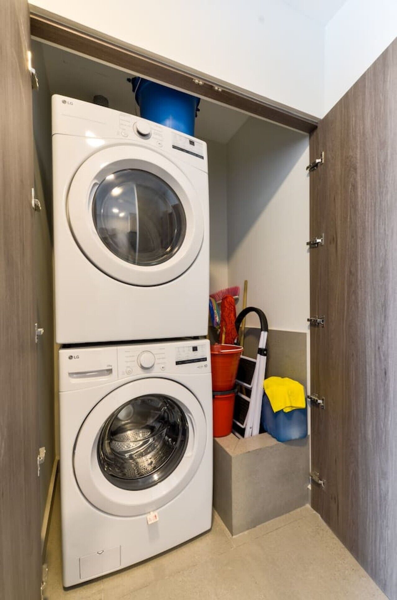 A laundry room with two stacked washing machines, a red bucket, and a yellow towel.