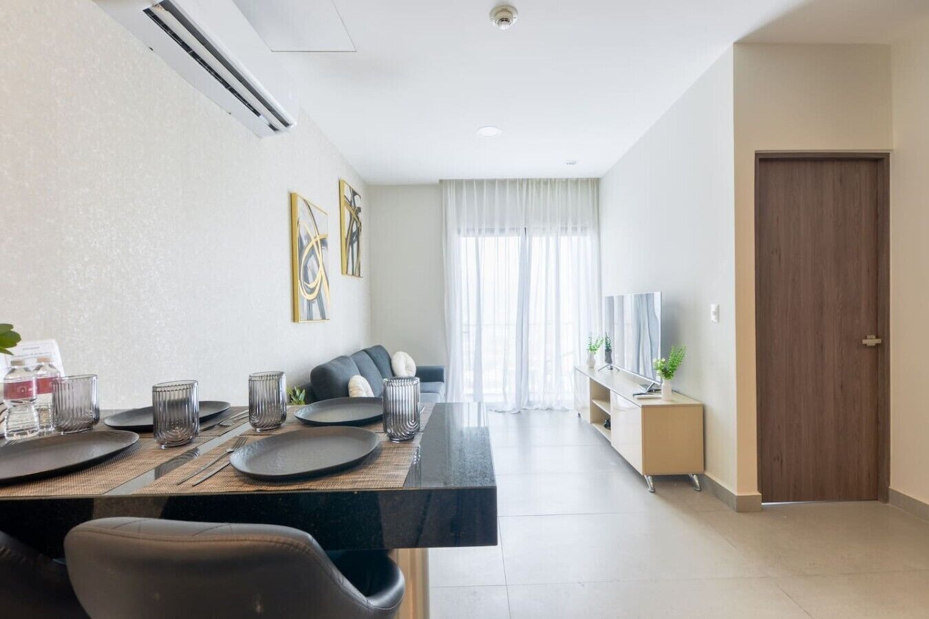 A modern dining area with a long table, chairs, and a television on a stand.
