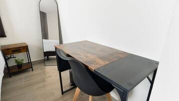 A modern room with a wooden desk, black chairs, a small wooden side table with a plant, and a large mirror on the wall.
