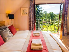 Une chambre d’hôtel avec un lit, une table de chevet, une lampe, une fenêtre donnant sur un jardin et un tableau au mur.