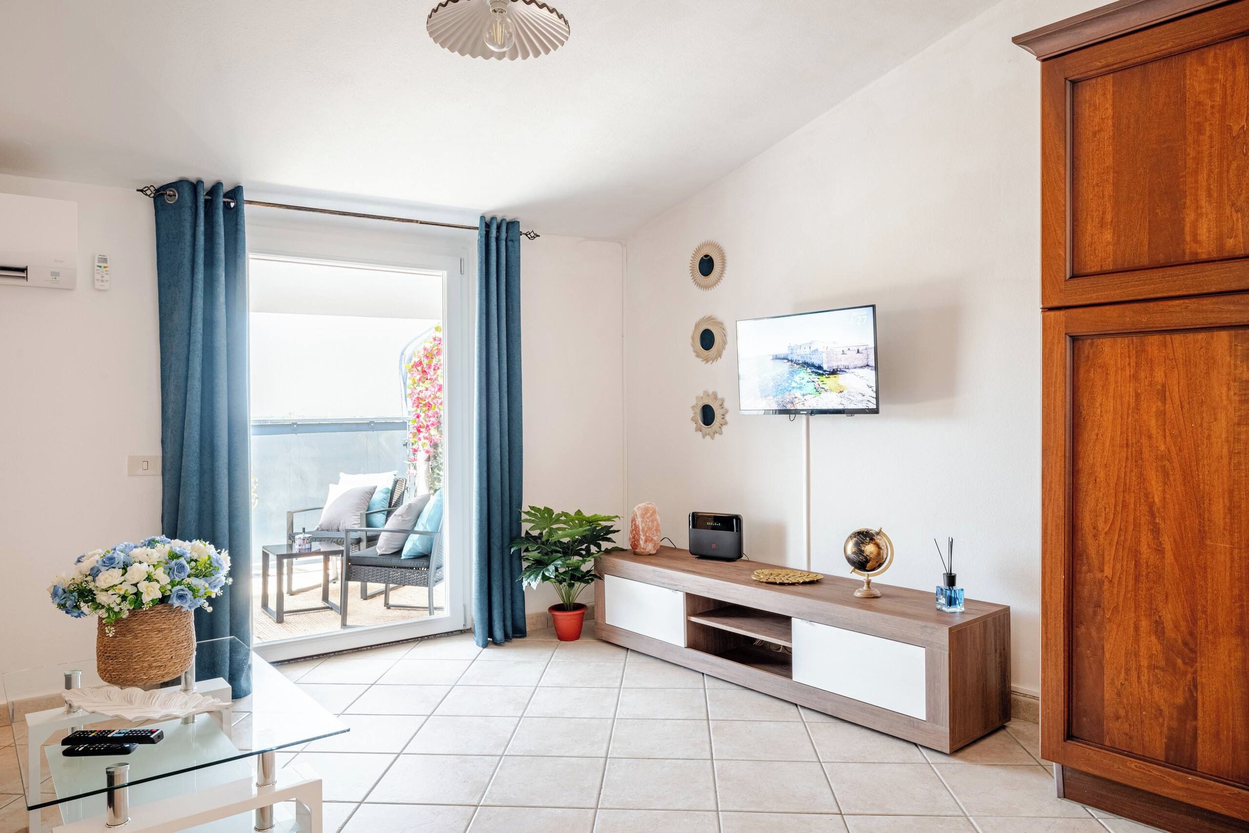 A modern living room with a TV, wooden cabinet, and a balcony with a chair and table.