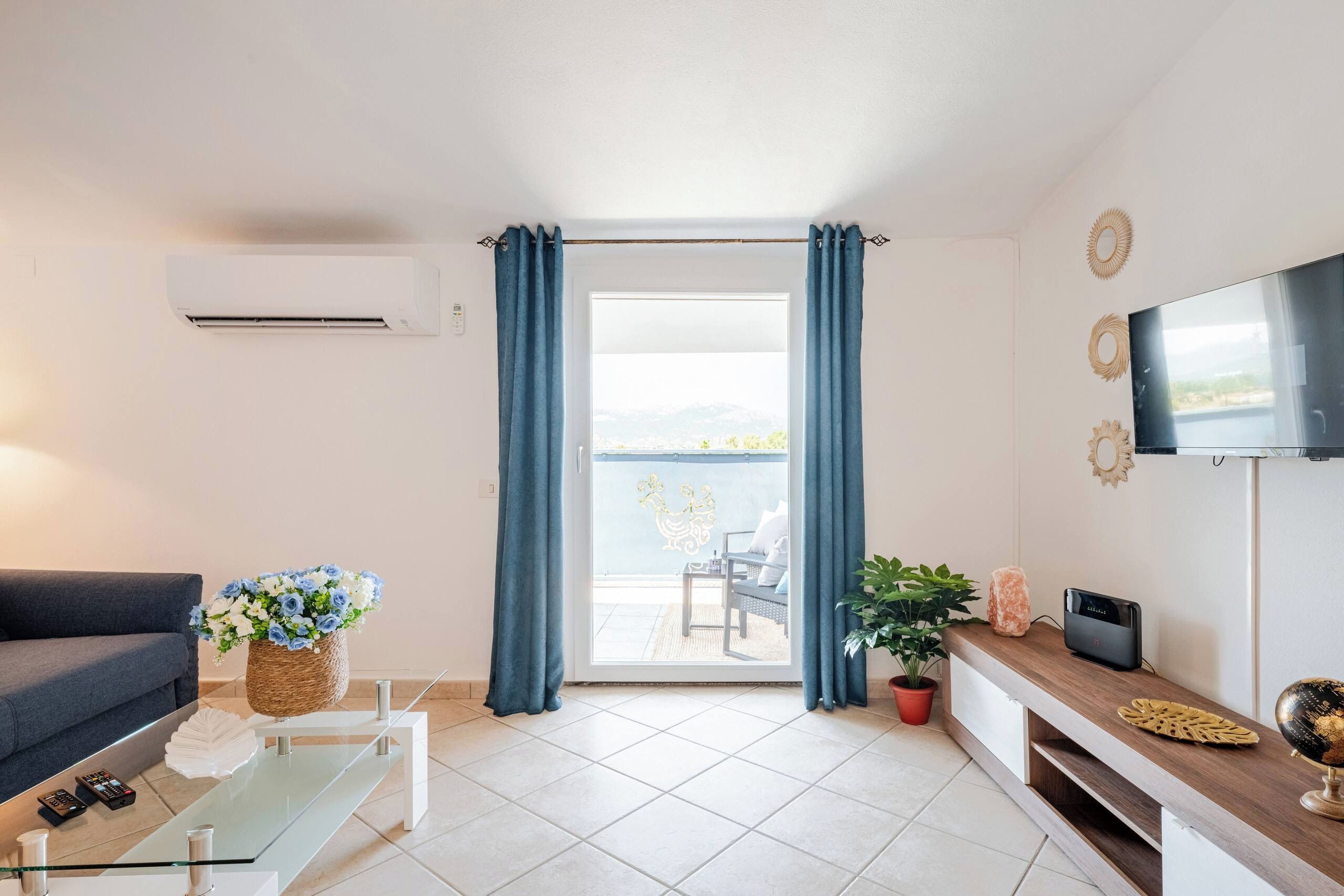 A modern living room with a sofa, a glass coffee table, a TV, and a balcony with a view.