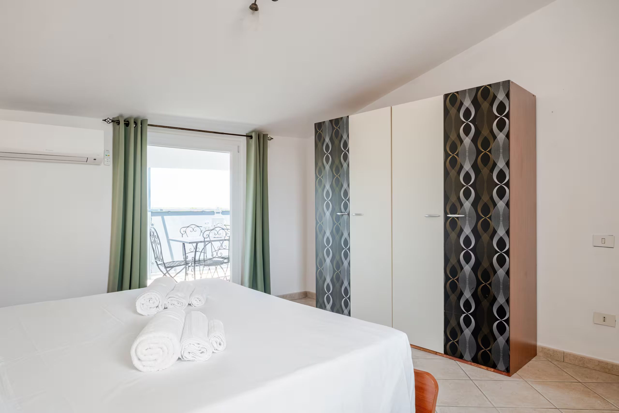 Ein Hotelzimmer mit Bett, einem Balkon mit Tisch und Stühlen sowie einem Schrank mit verzierten Türen.